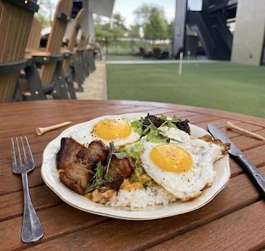 A brunch plate with fried eggs, rice, and pork belly on the Fairways at GLC patio